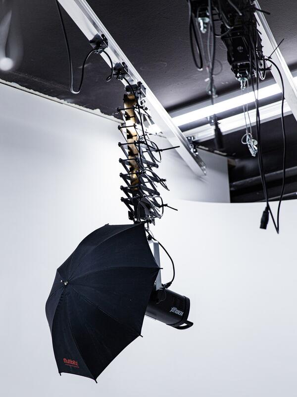 Fotostudio, Beleuchtungen mit Schirm hängen von der Decke, weiße Wand dahinter