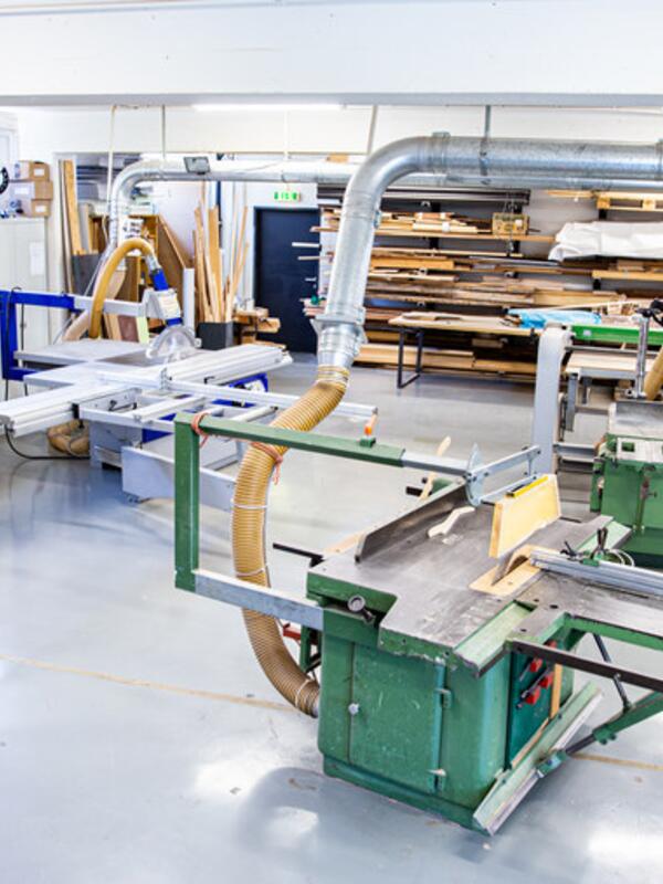 Holzwerkstatt, grüne Maschinen zur Holzbearbeitung, dahinter Holz in verschiedenen Formaten