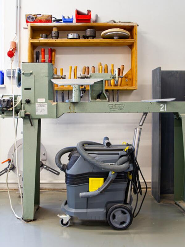 Holzwerkstatt mit Werkbank, dahinter Regal mit Werkzeug