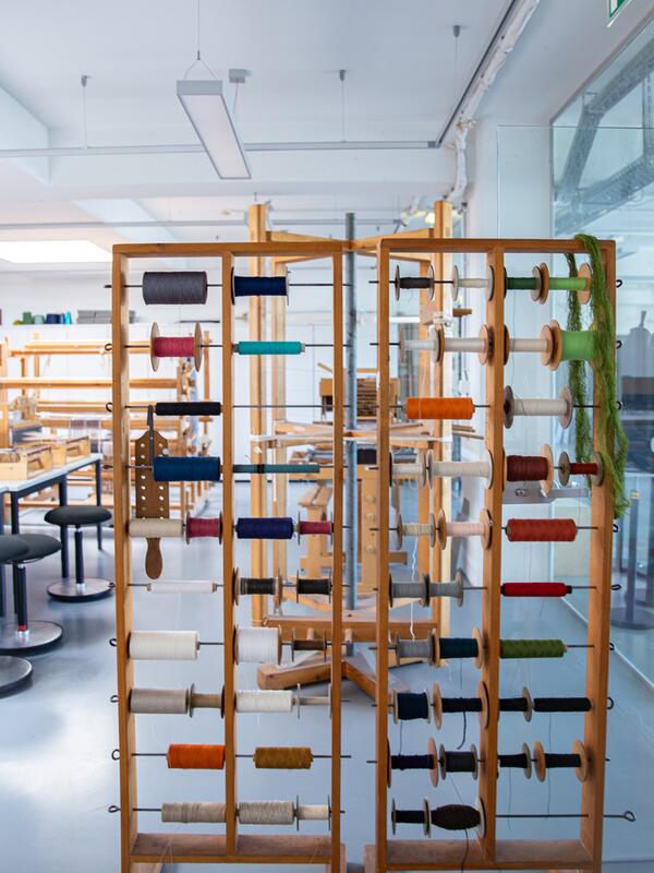 Weberei, Gestell mit Spindeln, dahinter Webstühle