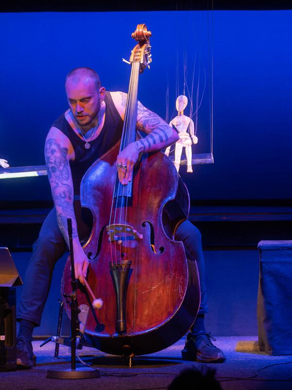Musiker mit Kontrabass, neben ihm zwei Holzmarionetten | © Christian Schneider