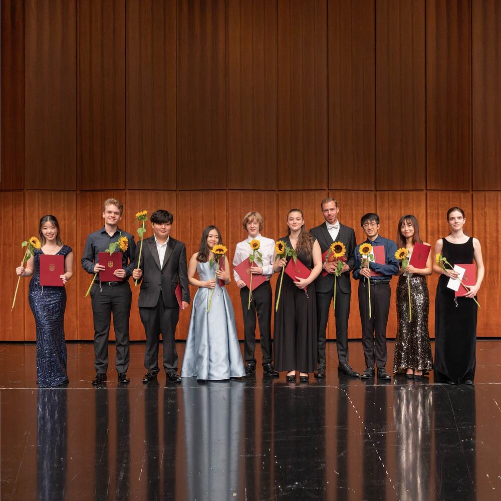 Mehrere Musiker*innen nebeneinander auf der Bühne, mit Sonnenblumen in der Hand | © Christian Schneider
