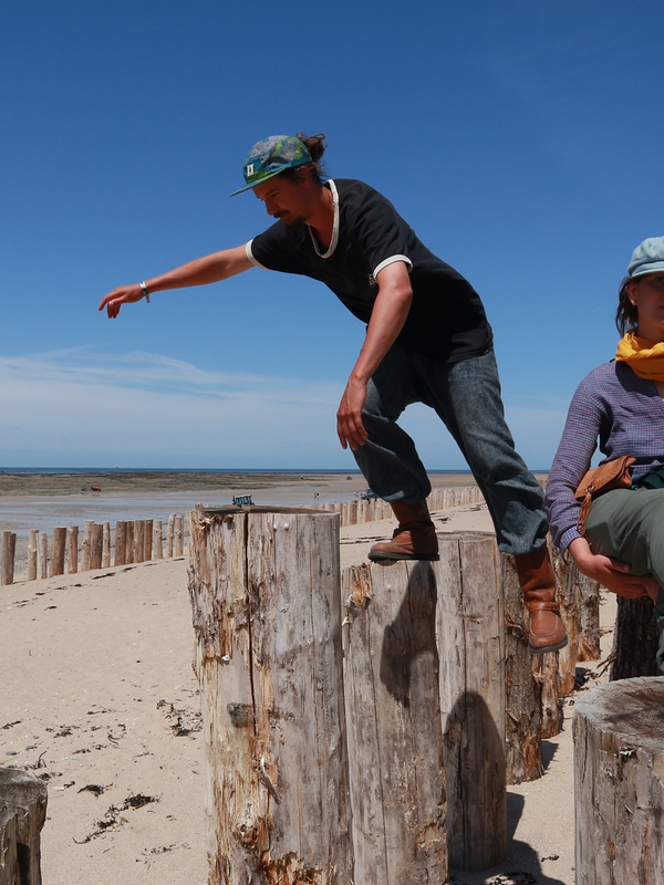 Lukas Stangl & Lara Schnepf an einem Strand, balancieren auf großen Holzpfosten