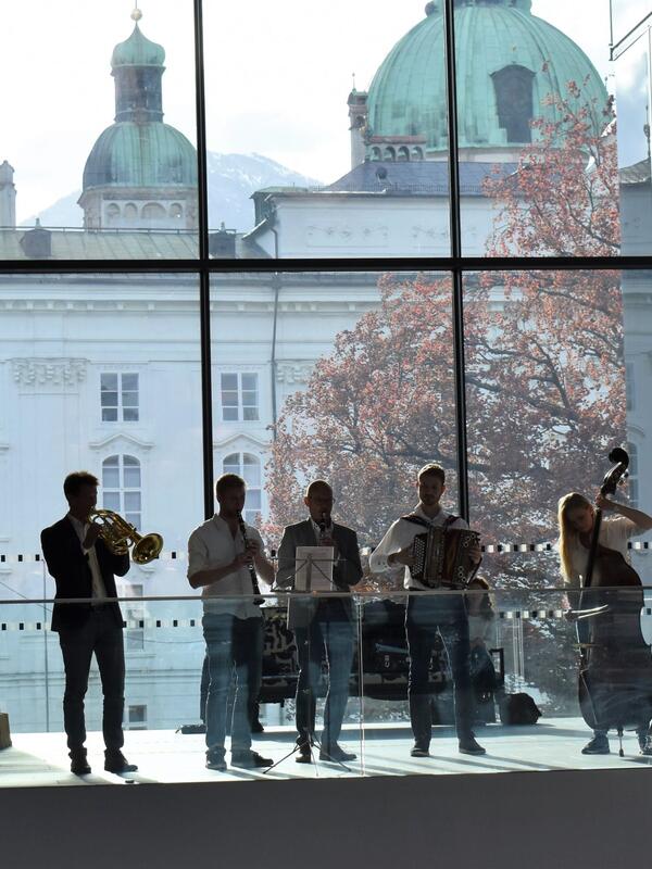 Fachdidaktik-Tagung 2018 | © Musikpädagogik Innsbruck Musiker*innen mit Akkordeon, Kontrabass, Harfe, Trompete und Klarinette stehen in einem großen offen Durchgang des Haus der Musik, große Fenster dahinter, Blick auf die Türme einer Kirche | © Musikpädagogik Innsbruck