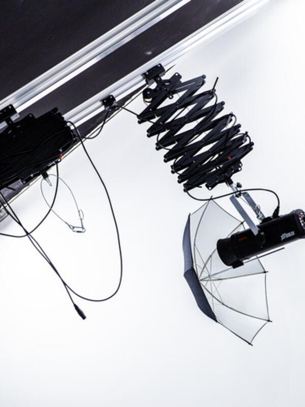 Fotostudio, Beleuchtungen und ein Schirm hängen auf einer Stange, weiße Wand dahinter
