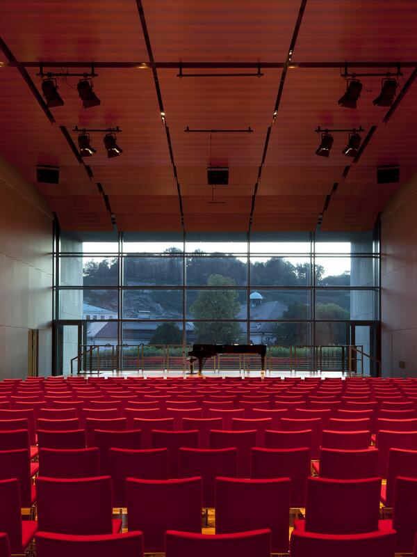 © Andrew Phelps Konzertsaal, rote Bestuhlung, Blick nach vorne, große Fensterfront, auf der Bühne ein Piano | © Andrew Phelps