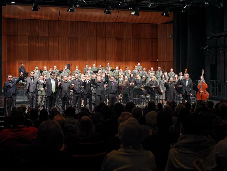 Viele Musiker*innen auf einer Bühne, stehend, Blick zum Publikum | © Christian Schneider