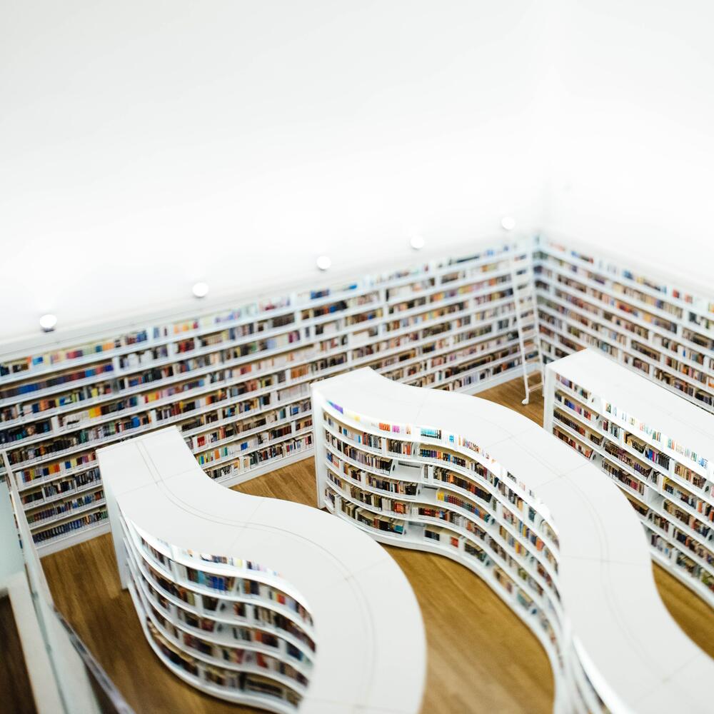 Weiße, geschwungene Bücherregale einer Bibliothek von oben fotografiert | © CHUTTERSNAP on Unsplash