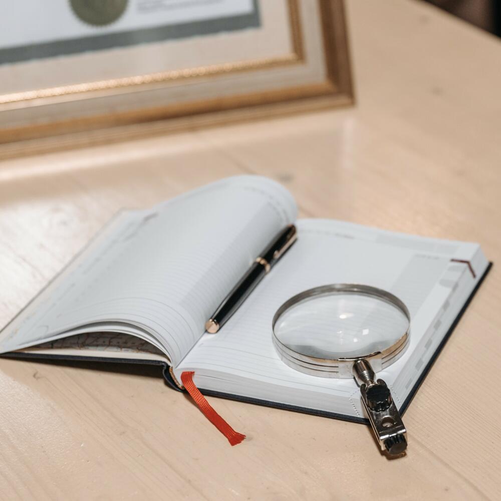 Buch liegt aufgeschlagen auf einem Tisch, darauf liegt eine Lupe | © Pavel Danilyuk